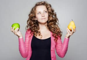 Woman comparing a green apple and a yellow pear.