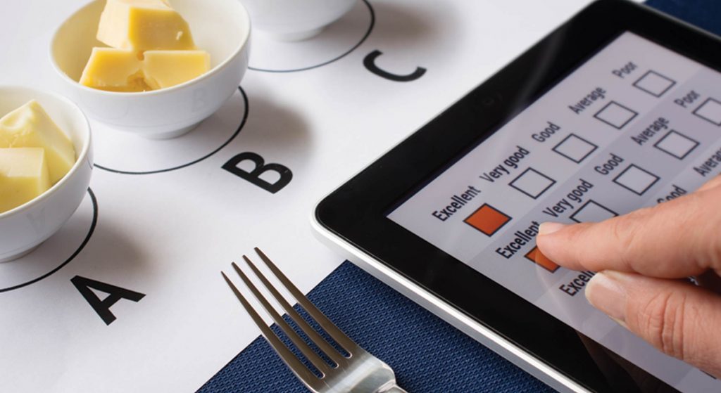 test1 Person taking a digital taste test survey on a tablet next to cheese samples labeled A, B, and C.