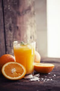 A freshly poured glass of orange juice with halved oranges on a wooden table.