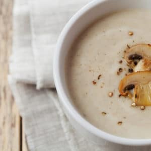 White bowl of creamy mushroom soup garnished with sliced mushrooms and pepper.